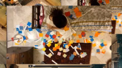 Decorative colour image of a figure on a bed with pieces of coloured paper surrounding them as seen from above.