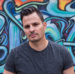 A portrait of Paul Watkins standing in front of a graffiti wall