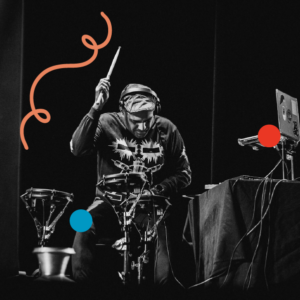 Ravish Momin performing with an electric drumkit and laptop on stage. Image is filtered in greyscale with colourful dots and a squiggly line added.