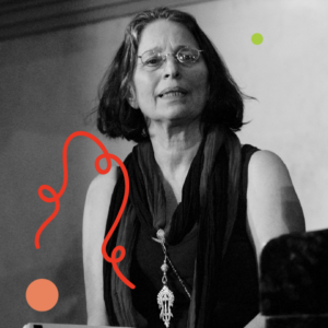 A photo of Patricia Nicholson speaking in a dimly lit space. Photo by Ken Weiss. Photo is filtered in greyscale with colourful dots and a squiggly line added.