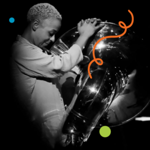 Julie Richard in profile against a dark background, holding a sousaphone and smiling.