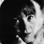 Black and white photo of Marilyn Crispell resting her face on her hand and looking into the camera.