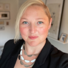 A photo of Dr. Sharon D. Engbrecht taken against a background of white walls with framed artwork, forming a corner behind them.