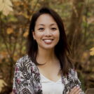 A head and shoulders portrait of Amy Hwang outdoors against a background of foliage.