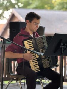 A photo of Hayden Mesnick seated and playing the accordion.