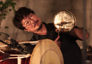 A photo of Dong-Won Kim playing percussion instruments with a small mallet. Photo by Liz Suenaga.