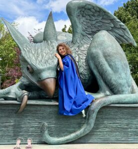 A photo of Dr. Shaghayegh Yassemi in graduate robes posing with the Gryphon statue at the University of Guelph.