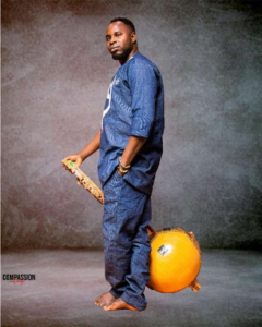 A photo of Siaka Diabate in blue clothing holding a kora between his legs and standing in profile against a grey background.